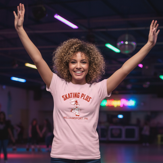 Woman wearing a pink t-shirt with 'Skating Plus' text and graphics, arms raised in an indoor setting.